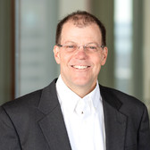 man with brown hair and glasses wearing a white shirt and black blazer